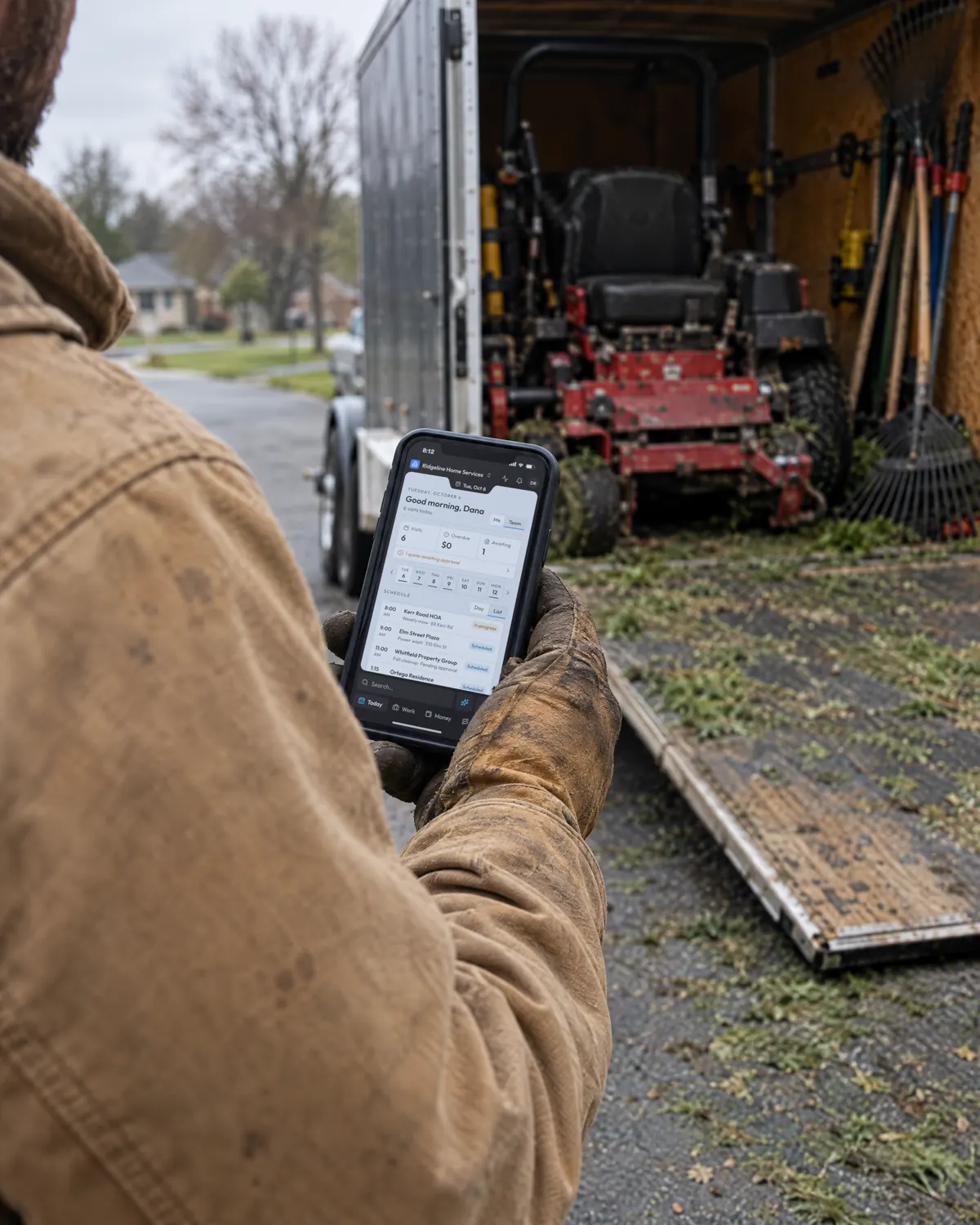 A landscaper at an open work trailer with OneTool’s Today screen on his phone, the Kerr Road HOA weekly mow in progress